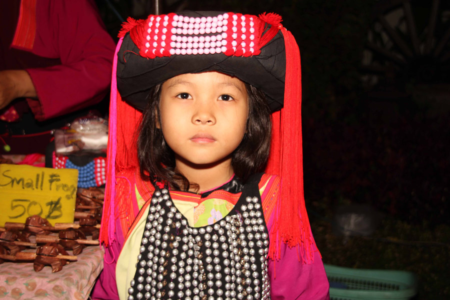 100 - Young Thai girl at market stall with serious look, wearing Thai costume.